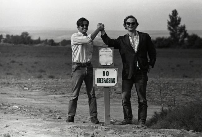 Guadalupe Gamboa, left, and Michael Fox clasping hands in a victory pose. Their hands are above a No Trespassing sign on Rogers Walla Walla labor camp. Rogers Walla Walla Labor Camp. Walla Walla, Wash. (1971).