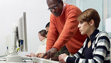 A tall black man assists a young woman with a computer