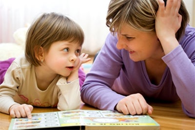 A mother and young girl read a book together while lying on the floor.