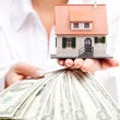 person holding model home and money