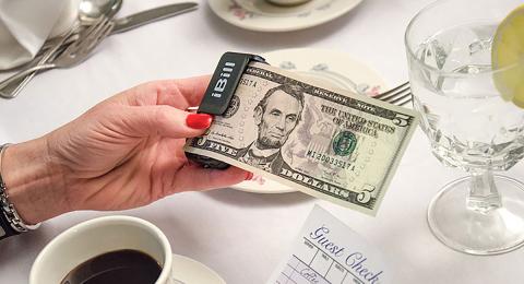 A woman holds an iBill reader with a $5 bill at a restaurant