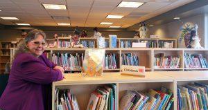Woman leaning on a low bookshelf in a library.