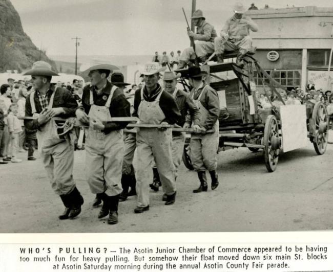 Black and white photo of men pulling a float