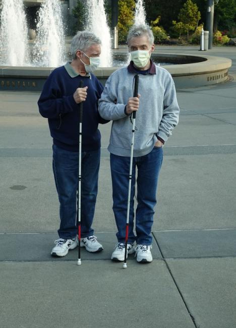 two men standing together with white canes in front of a fountain