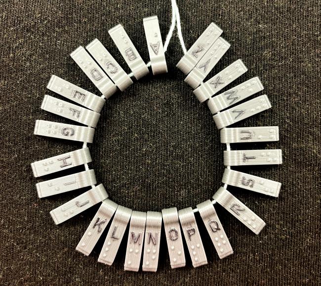 Held together on a string, 24 individual braille stamps for letters a through z
